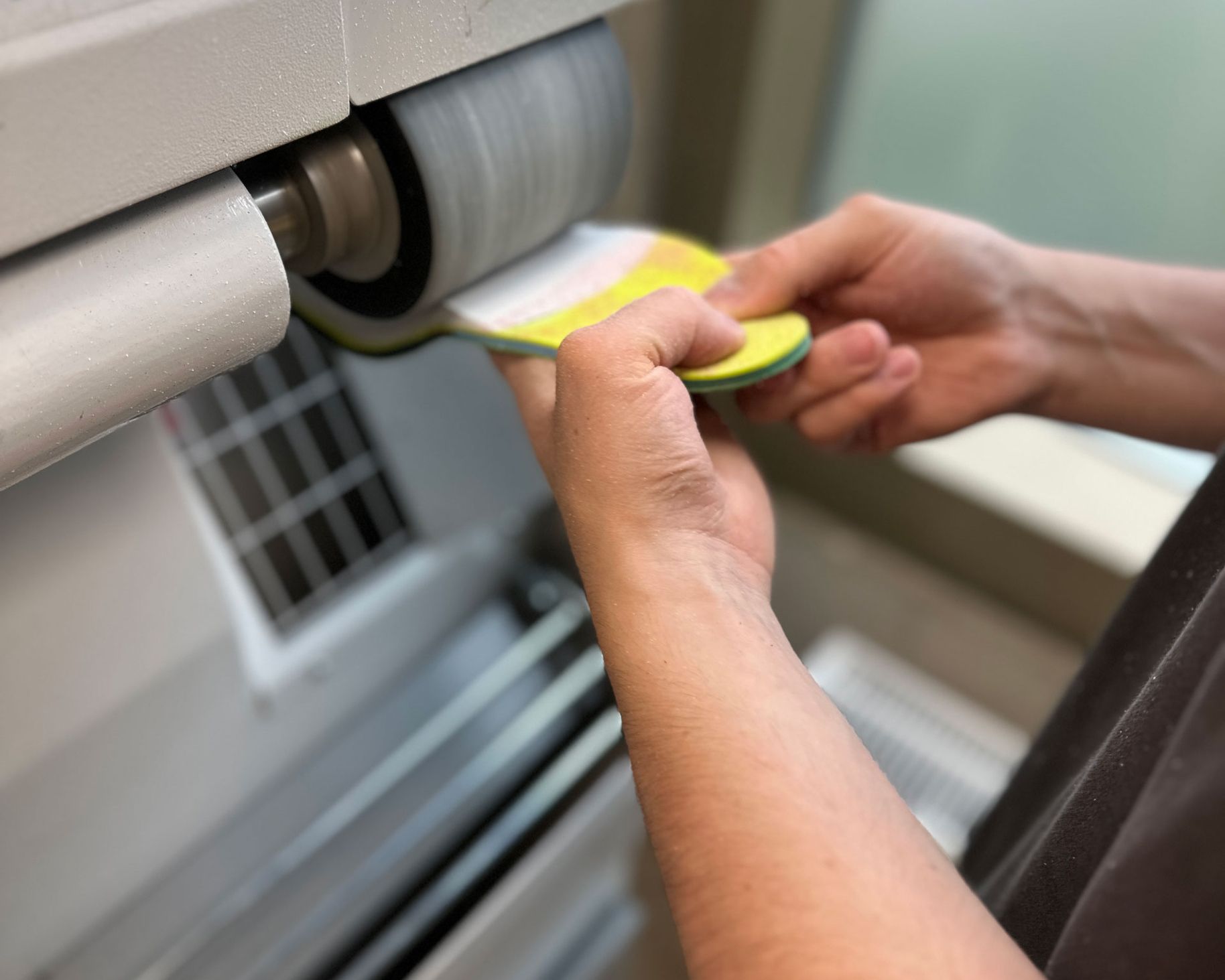 Eine Person hält eine grüne Einlage mit einer Hand, während sie mit der anderen Hand eine Schleifmaschine bedient. Die Schleifmaschine hat eine rotierende Walze.
