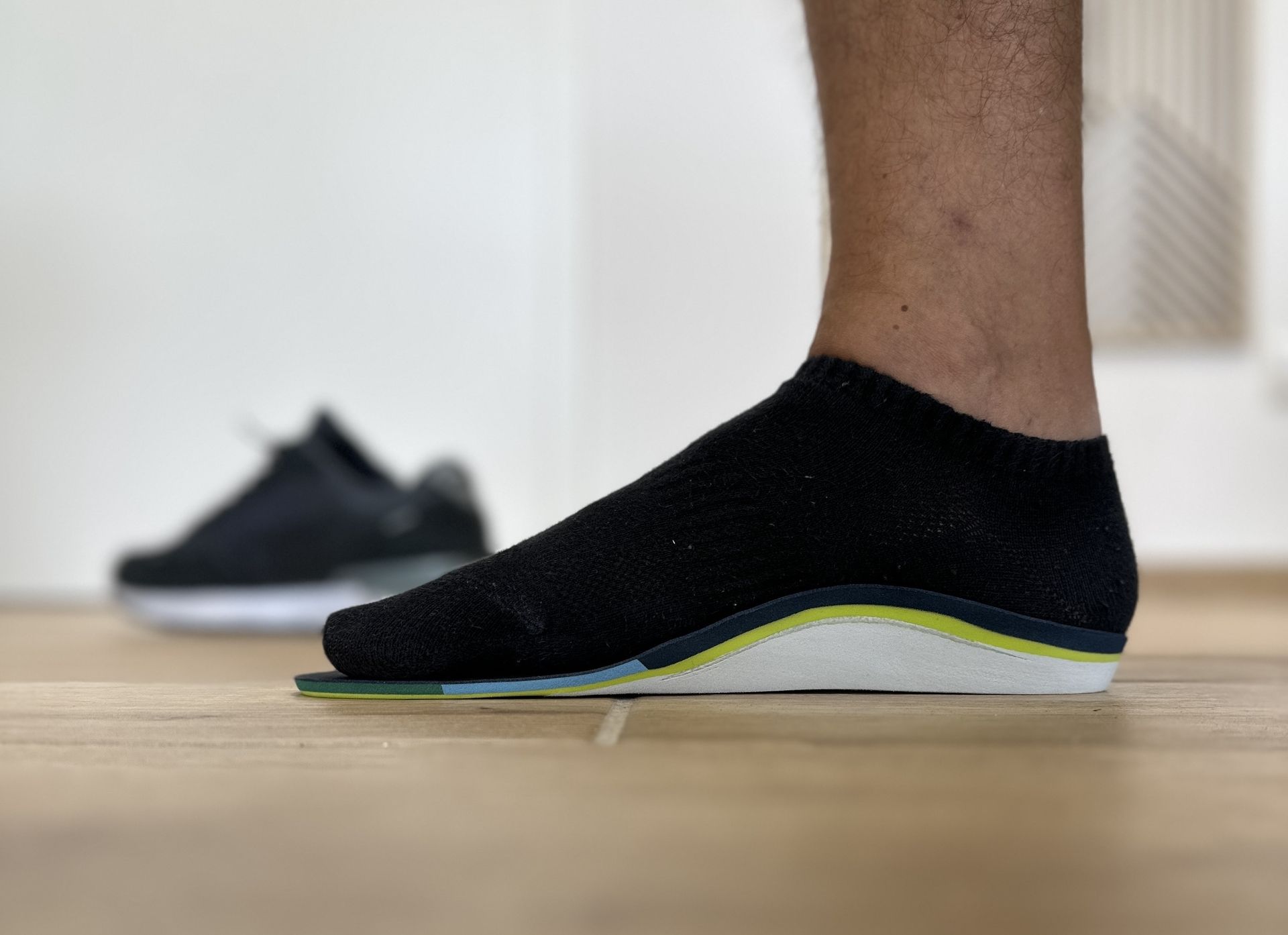 Fuß mit schwarzer Socke auf orthopädischer Einlage mit grüner und grauer Schicht auf Holzboden