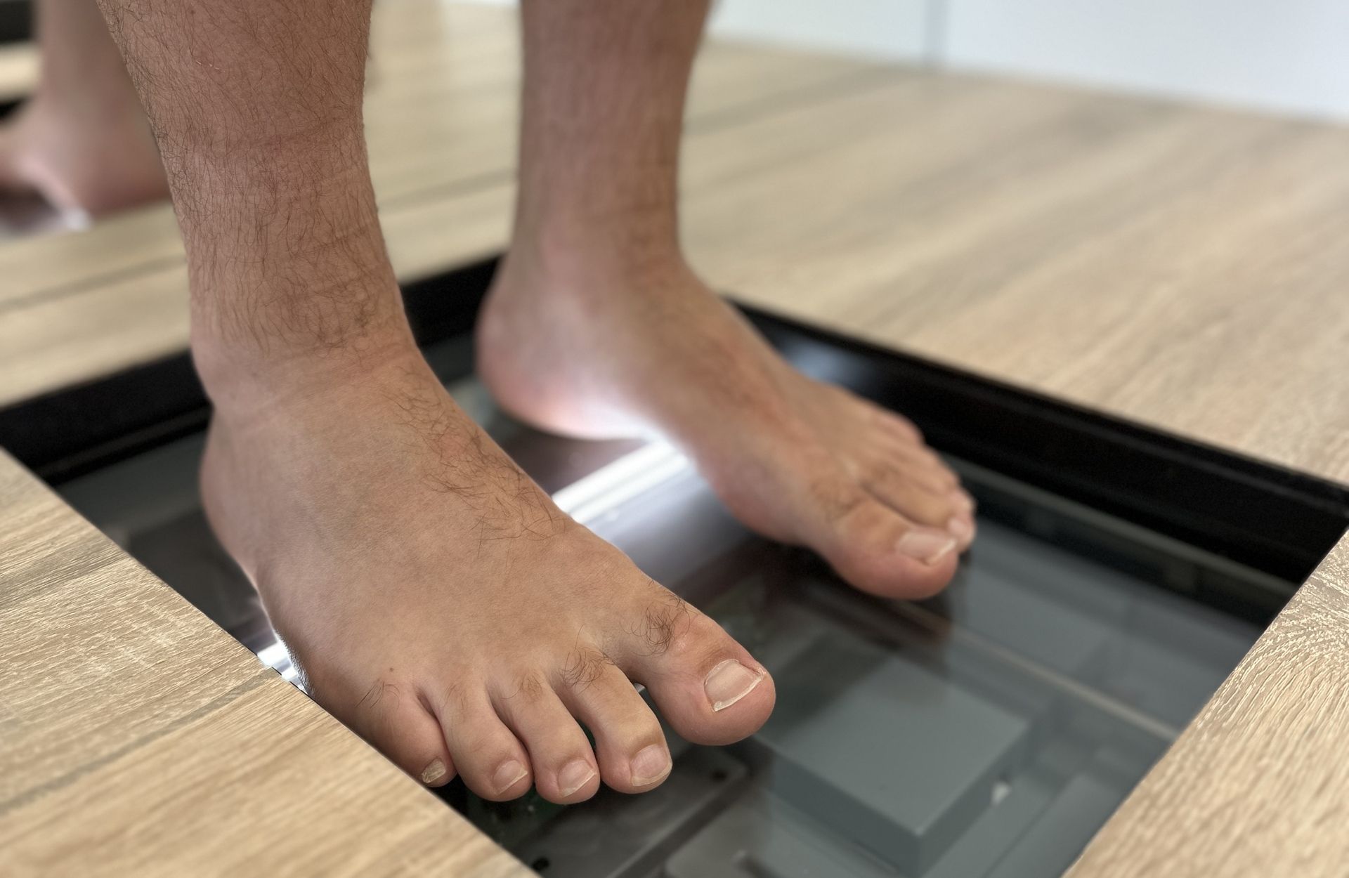 Barfuß stehende Füße auf einer Glasplatte im Holzfußboden mit sichtbarer Technik darunter