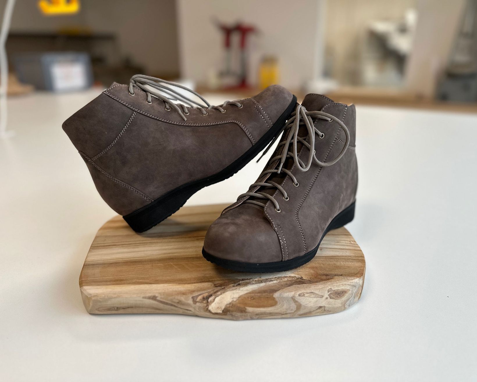 Braune Stiefeletten aus Wildleder mit Schnürung, auf einem Holzbrett platziert. Die Schuhe haben eine runde Zehenform und eine flache Sohle.