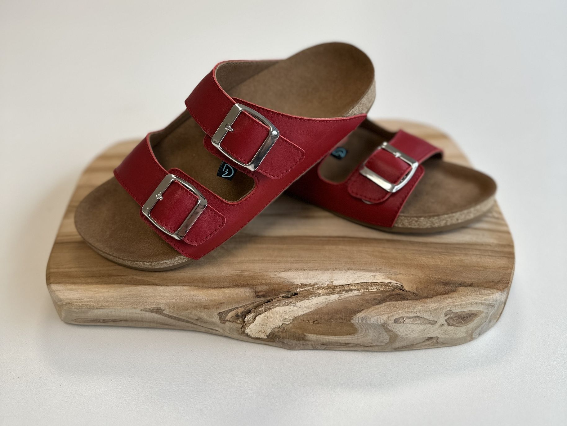 Rote Sandalen mit zwei verstellbaren Schnallen auf einem Holzbrett