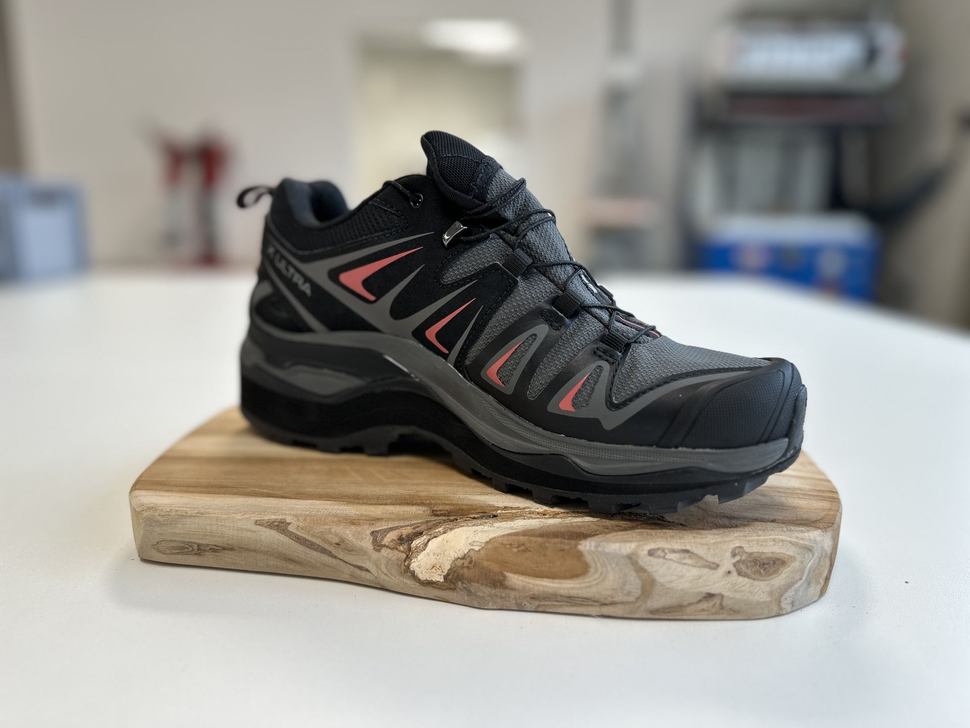 Schwarzer Wanderschuh mit grauen und roten Akzenten auf Holzbrett, unscharfer Hintergrund